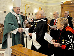 Archbishop Joseph W. Tobin stops to shake hands with Dr. Hans Geisler during the opening procession of an Oct. 14 Mass in the Blessed Sacrament Chapel of SS. Peter and Paul Cathedral in Indianapolis. The Mass celebrated the 900th anniversary of the formal founding of the Order of Malta, an order of lay Catholics that serves the sick, disabled and people in need. Geisler and his wife, Margie, right, are wearing the order’s habit. They are members of St. Luke the Evangelist Parish in Indianapolis. Also attending the Mass and standing behind Geisler are John Fink, editor emeritus of The Criterion, and George Maley, a member of the order. (Photo by Sean Gallagher)