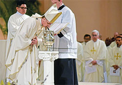 Archbishop Charles C. Thompson ritually breathes into chrism oil on April 4, Tuesday of Holy Week, at SS. Peter and Paul Cathedral in Indianapolis during the annual archdiocesan chrism Mass. Assisting at the Mass are transitional Deacon Jose Neri, left, and seminarian Samuel Hansen. (Photo by Sean Gallagher)